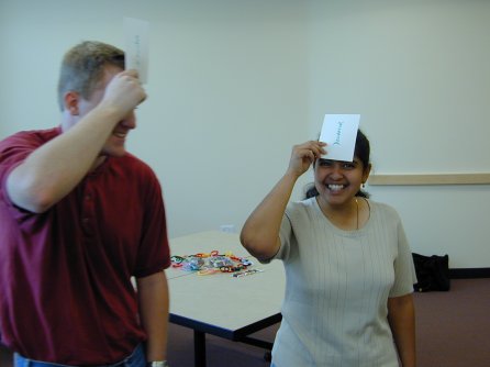 A pair of people standing, holding cards against their foreheads