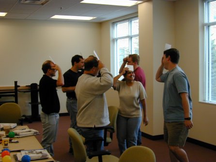 A group of six people standing, holding cards against their foreheads