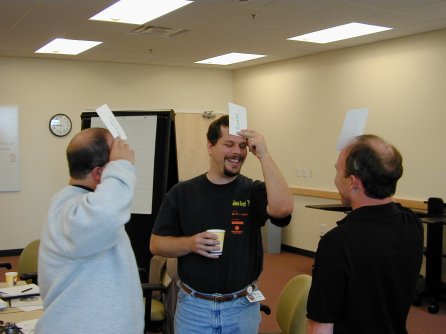 A group of three people standing, holding cards against their foreheads