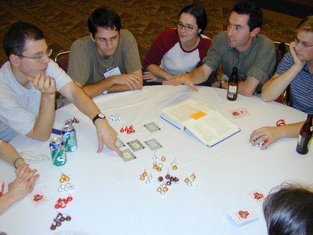 five people sitting at a round table with cards and candy