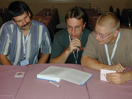 three people looking at a book and their hand of cards