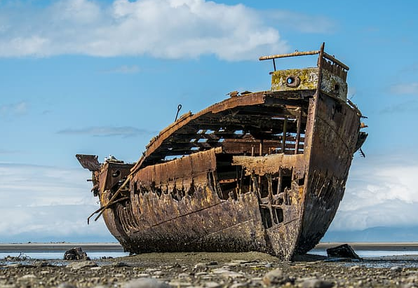 An aged boat aground on the beach, that has a deteriorated structure.