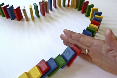 image of a line of dominoes being interrupted by a human hand