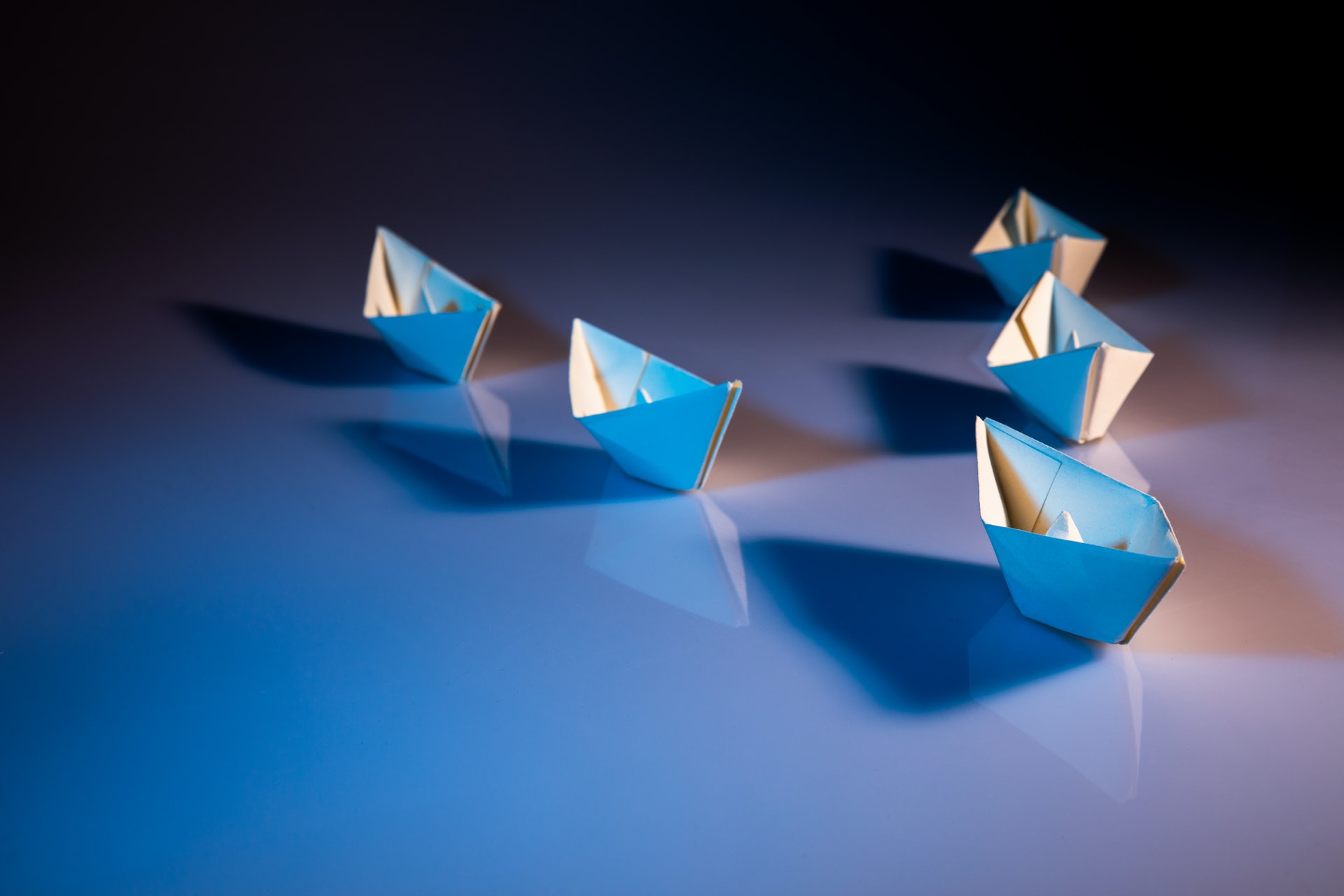 Five folded paper boats, arranged in a V shape on a flat counter