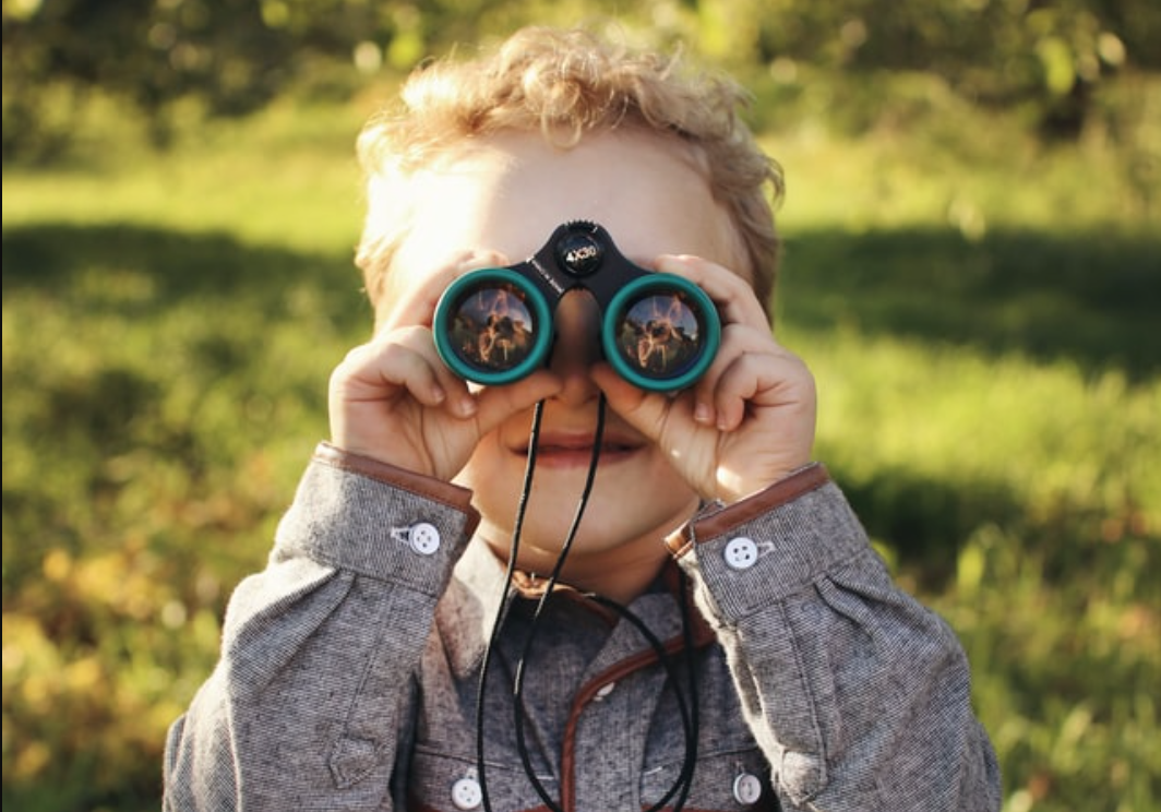 A small child with blond hair looking through binoculars, facing forward