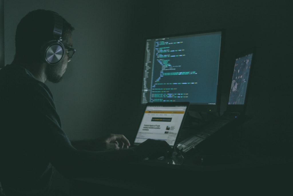 person wearing headphones in front of three monitors in the dark