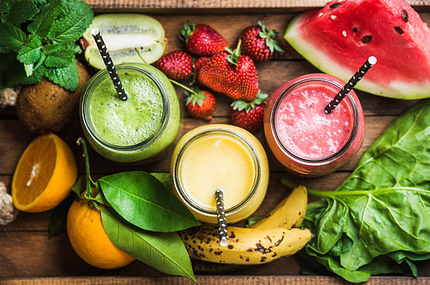 Three smoothies with straws, on a tray with fruit.