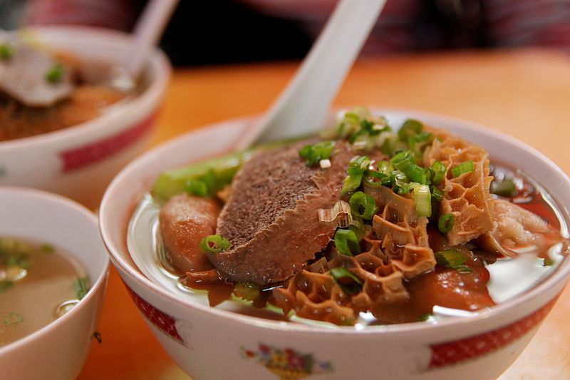 A bowl of broth with pieces of tripe, beef, and green onions.